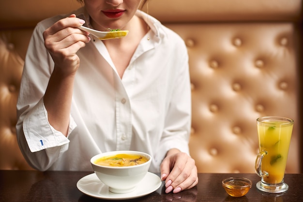 Giovane femmina in bianco che mangia minestra crema saporita.