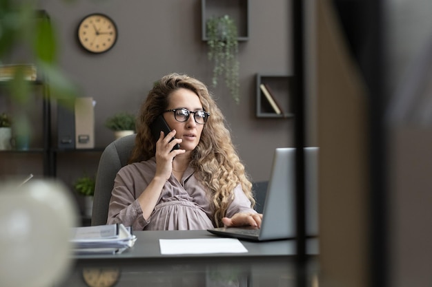 Giovane femmina incinta in vestito grigio che parla dal telefono cellulare