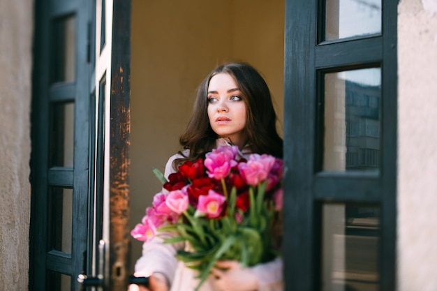 Giovane femmina sveglia con i fiori che aprono porta e che guardano fuori