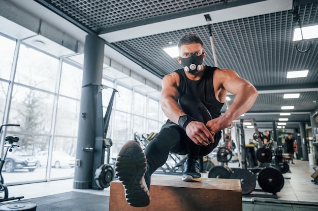 Giovane forte in abiti sportivi e maschera spaventosa che fa flessioni su una gamba in palestra