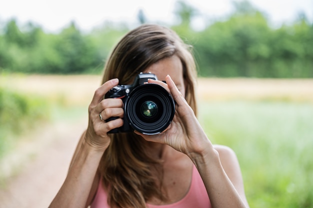 Giovane fotografa che scatta una foto direttamente a te in piedi fuori nella natura.