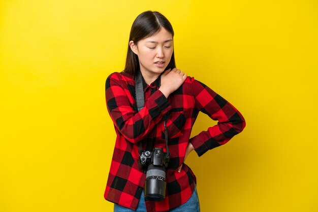 Giovane fotografa cinese isolata su sfondo giallo che soffre di dolore alla spalla per aver fatto uno sforzo