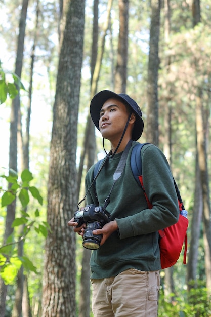 Giovane fotografo asiatico con la macchina fotografica in mano e guardando lontano in una foresta