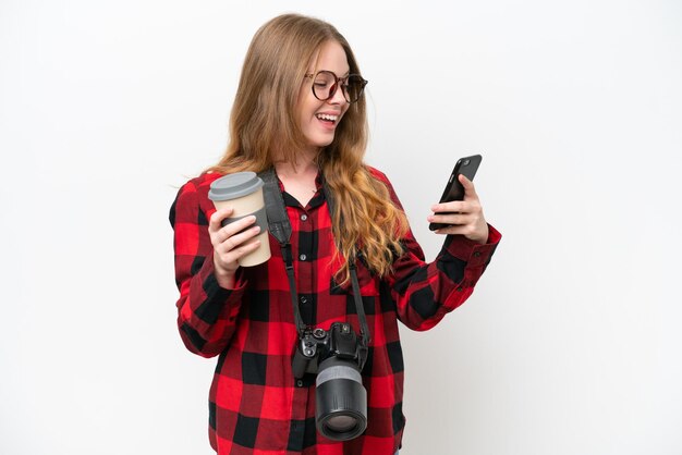 Giovane fotografo bella donna isolata su sfondo bianco tenendo il caffè da portare via e un cellulare