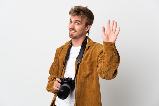 Giovane fotografo biondo uomo isolato su sfondo bianco salutando con la mano con felice espressione