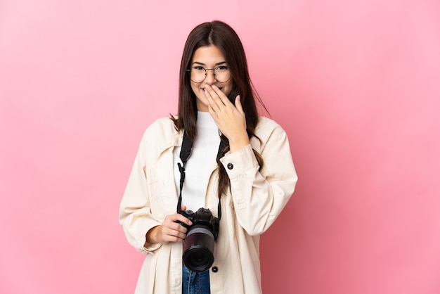 Giovane fotografo brasiliano ragazza isolata sulla parete rosa felice e sorridente che copre la bocca con la mano