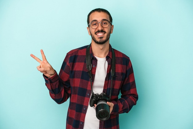 Giovane fotografo caucasico uomo isolato su sfondo blu gioioso e spensierato che mostra un simbolo di pace con le dita.