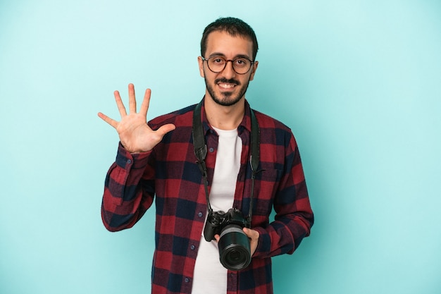 Giovane fotografo caucasico uomo isolato su sfondo blu sorridente allegro che mostra il numero cinque con le dita.