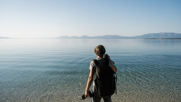 Giovane fotografo che fa una pausa la macchina fotografica e il treppiede della tenuta del mare