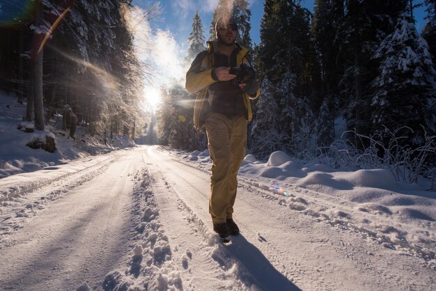 giovane fotografo che si gode la splendida natura invernale mentre si cammina su una strada di campagna innevata durante il tramonto o l'alba nella foresta con neve fresca