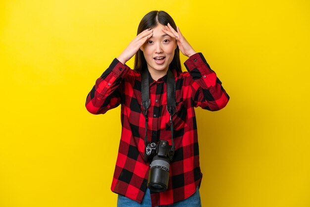 Giovane fotografo donna cinese isolata su sfondo giallo con espressione sorpresa