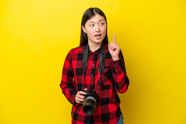 Giovane fotografo donna cinese isolata su sfondo giallo pensando a un'idea che punta il dito verso l'alto