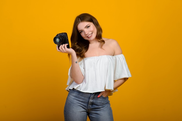 Giovane fotografo femminile con la macchina fotografica sopra fondo giallo