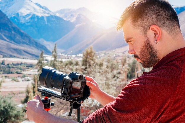 Giovane fotografo latino che guarda e tiene in mano una macchina fotografica all'aperto su una valle Valle dell'Elqui