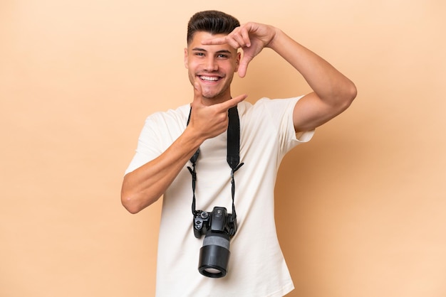 Giovane fotografo uomo caucasico isolato su sfondo beige focalizzando il viso Simbolo di inquadratura