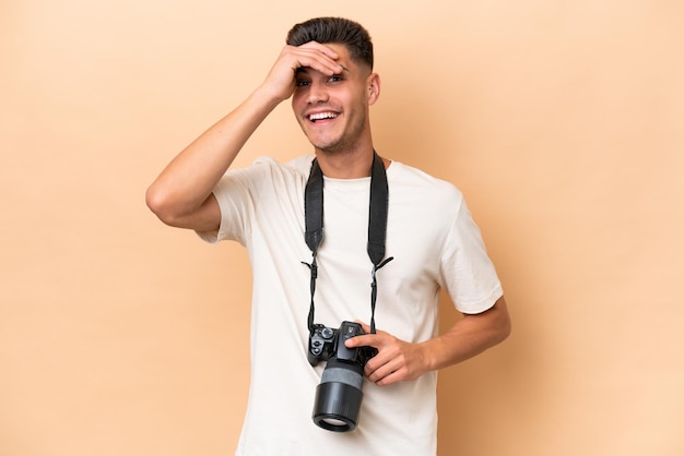 Giovane fotografo uomo caucasico isolato su sfondo beige guardando lontano con la mano per guardare qualcosa