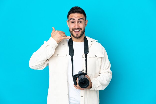 Giovane fotografo uomo isolato sulla parete blu che fa il gesto del telefono. Richiamami segno