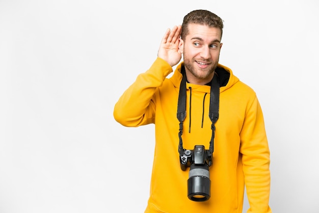 Giovane fotografo uomo su sfondo bianco isolato ascoltando qualcosa mettendo la mano sull'orecchio