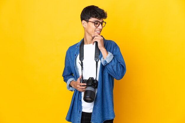 Giovane fotografo uomo su sfondo giallo isolato guardando al lato e sorridente