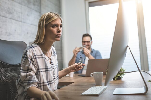 Giovane freelance femminile carina e pensierosa che lavora a un nuovo progetto in ufficio. Sta guardando un progetto su un computer.