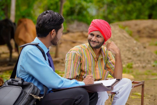 Giovane funzionario di banca dell'India che completa il lavoro di ufficio con l'agricoltore nella sua fattoria.