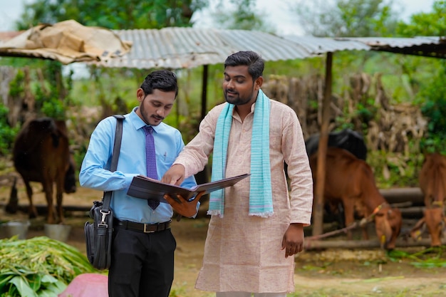 Giovane funzionario di banca dell'India che completa il lavoro di ufficio con l'agricoltore nella sua fattoria.