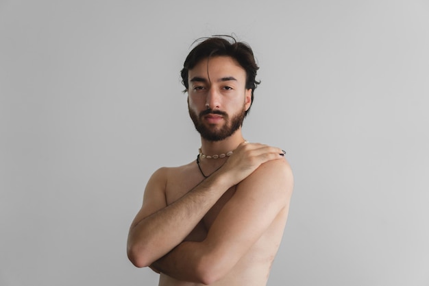 Giovane gay queer latino nudo che guarda con orgoglio la macchina fotografica mentre si prende cura di se stesso su uno sfondo bianco