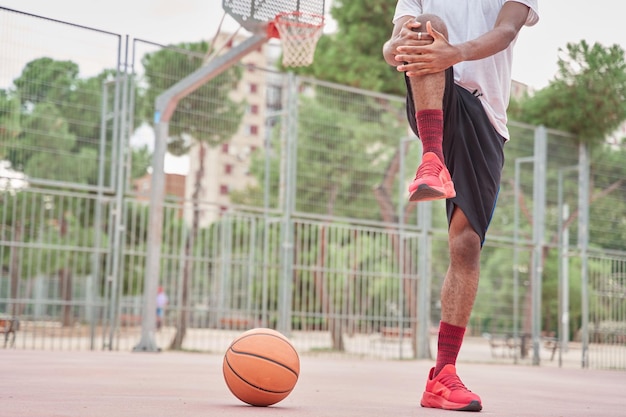 giovane giocatore di basket afroamericano irriconoscibile che allunga le gambe prima di giocare