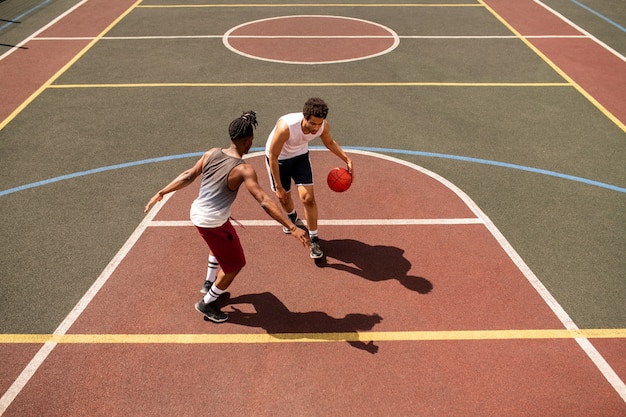 Giovane giocatore di basket che cerca di difendere la palla dal rivale mentre la trasporta lungo il campo all'aperto durante il gioco