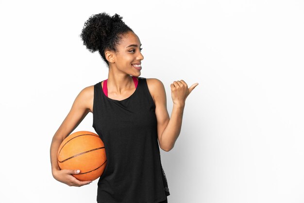 Giovane giocatore di basket donna latina isolata su sfondo bianco che punta al lato per presentare un prodotto