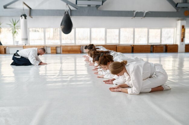 Giovane gruppo femminile di studenti di aikido e maestro che si saluta all'inizio della lezione. Corso di formazione di arti marziali per donna