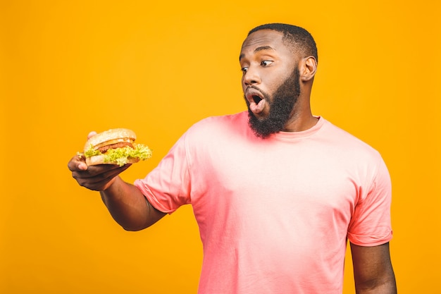 Giovane hamburger mangiatore di uomini afroamericano isolato sopra la parete gialla.