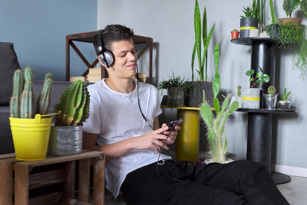 Giovane hipster alla moda in cuffia che ascolta musica, ragazzo adolescente con smartphone seduto a casa che si rilassa godendosi la musica