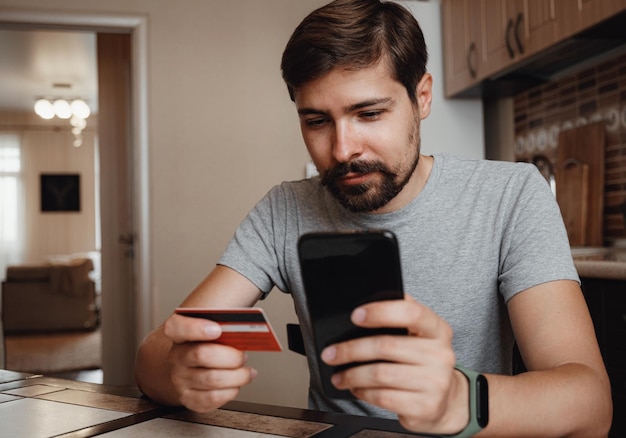 Giovane hipster che acquista online con carta di credito tramite smartphone a casa