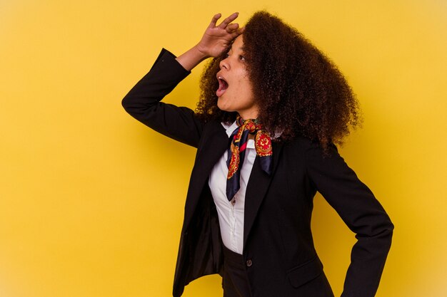 Giovane hostess afroamericana isolata sul giallo che guarda lontano tenendo la mano sulla fronte.