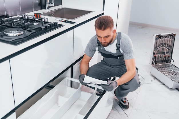 Giovane idraulico professionista in uniforme grigia che lavora in cucina