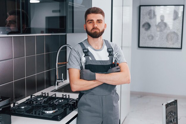 Giovane idraulico professionista in uniforme grigia in piedi sulla cucina