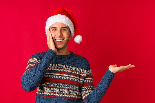 Giovane il giorno di Natale che sorride e che indica da parte, mostrando qualcosa nello spazio.