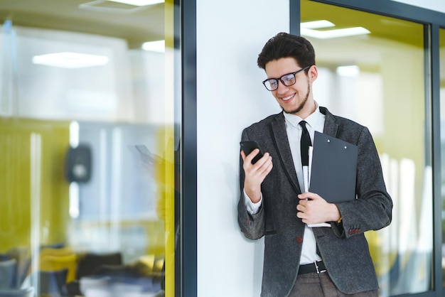 Giovane impiegato con gli occhiali utilizzando lo smartphone mobile L'uomo d'affari tiene il telefono in mano