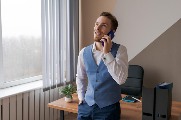 Giovane impiegato sta parlando sorridente sul telefono appoggiato al desktop