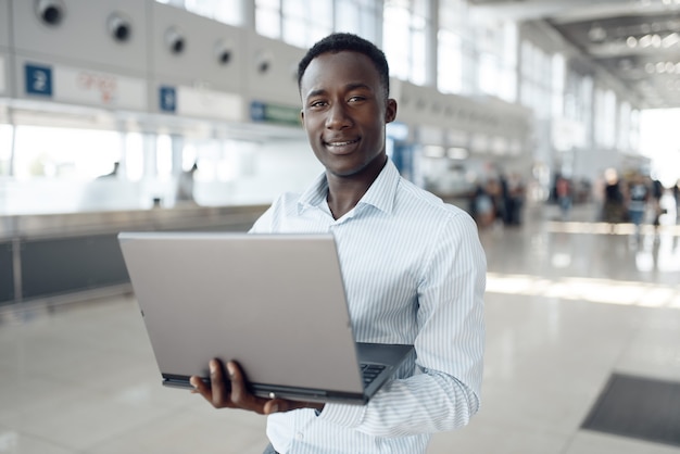 Giovane imprenditore afro che lavora al computer portatile in autosalone. Uomo d'affari di successo al salone dell'auto, uomo di colore in abbigliamento formale