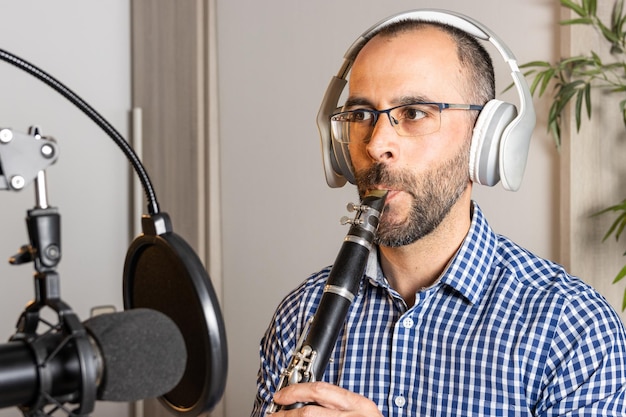 Giovane imprenditore che suona il clarinetto a casa e registra musica per trasmetterla in streaming online con il suo computer