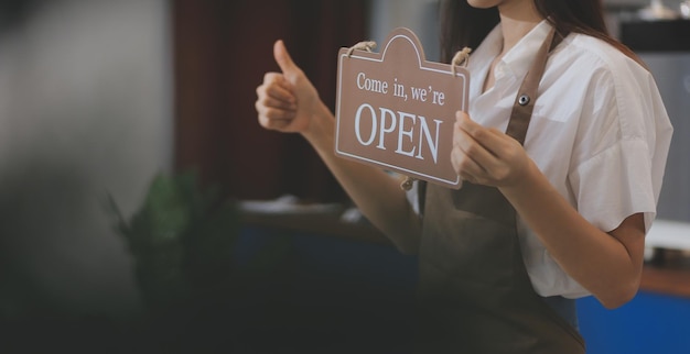 Giovane imprenditore che tiene segno aperto sulla porta di vetro al caffè