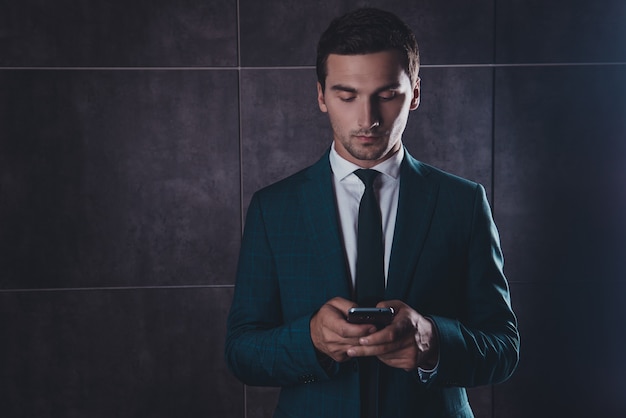 Giovane imprenditore concentrato in chat su smartphone su uno spazio grigio