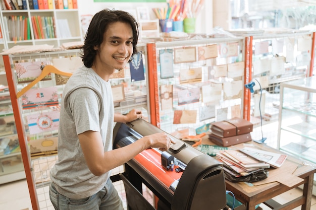Giovane imprenditore maschio che produce carta adesiva dalla macchina che lavora in una cartoleria