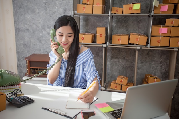 Giovane imprenditore parlando su un telefono mentre si siede alla sua scrivania in un ufficio a casa.