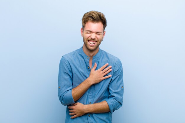 Giovane imprenditore ridere ad alta voce per uno scherzo divertente, sentirsi felice e allegro, divertirsi su sfondo blu