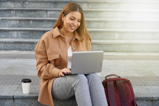 Giovane imprenditore. Studente universitario. Lavorando al computer portatile. Rete di computer. Seduti all'aperto. Studiare all'estero. Tazza da caffè da asporto.