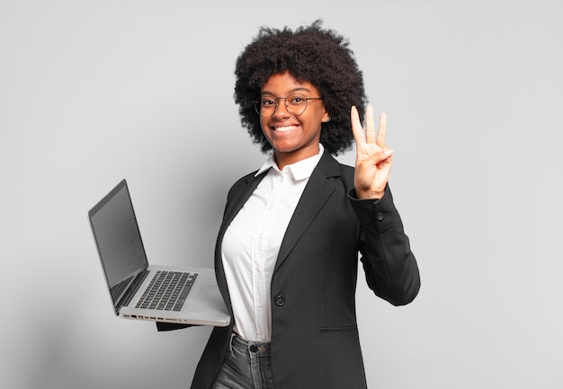 Giovane imprenditrice afro sorridente e dall'aspetto amichevole, mostrando il numero tre o il terzo con la mano in avanti, conto alla rovescia. concetto di business