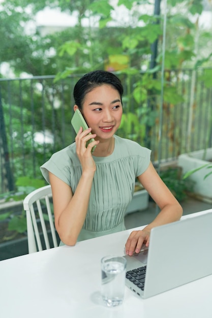 Giovane imprenditrice asiatica che parla al telefono mentre lavora in ufficio a casa